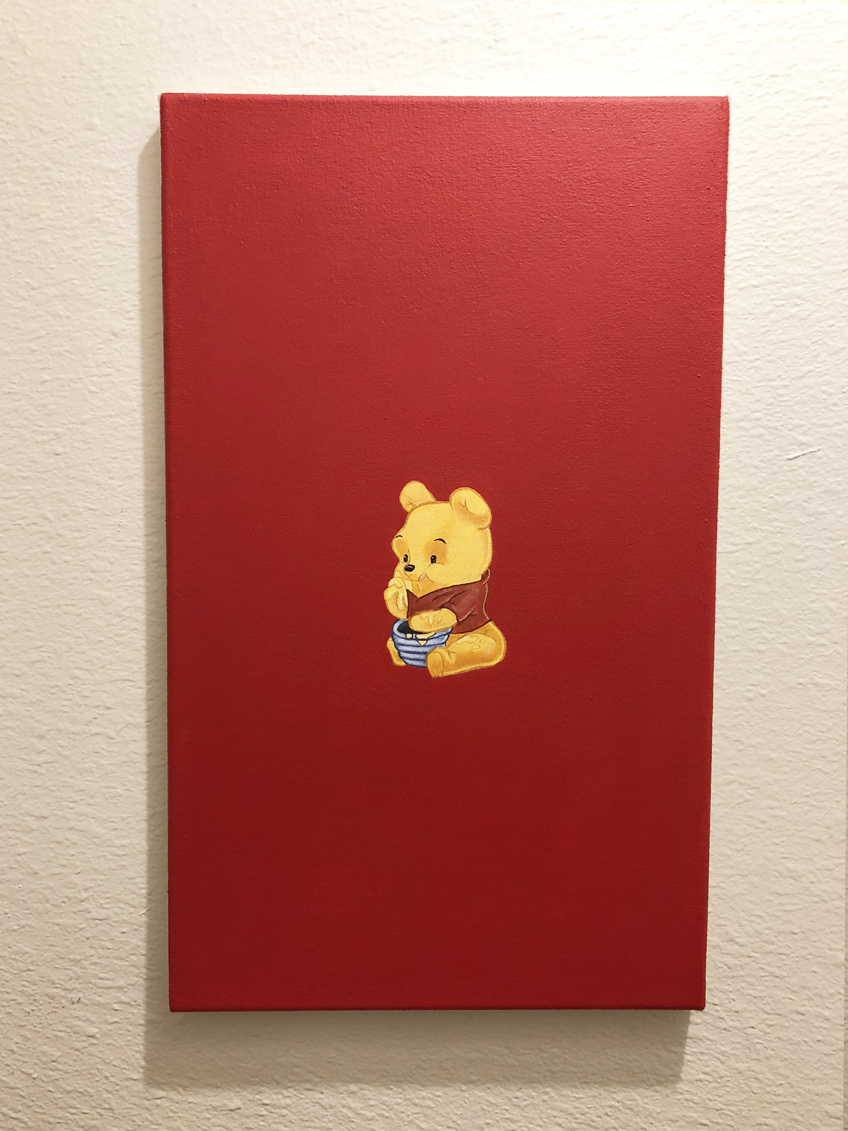 Painting of winnie the pooh eating honey out of a pot on a red background hung on a white wall